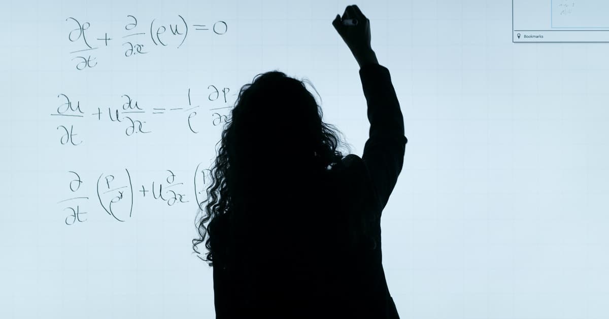 professora mulher de costas em frente a um quadro branco com formulas e fração