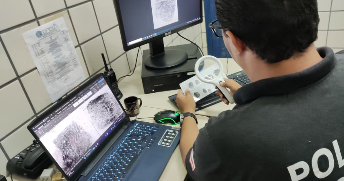 Papiloscopista fazendo análise de impressões digitais usando computadores e lupa